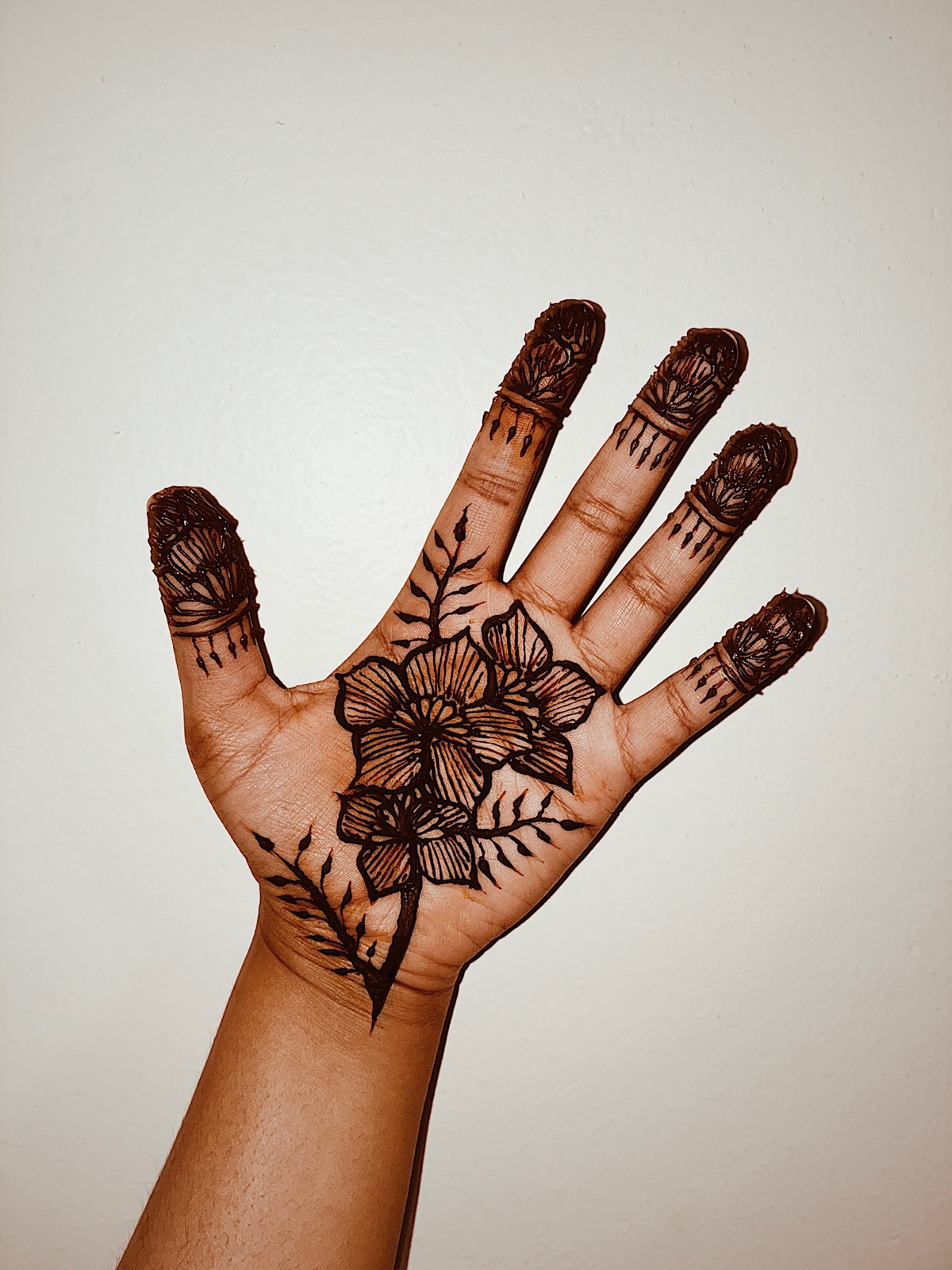 Palm-up henna with a central floral and striped fingertip caps